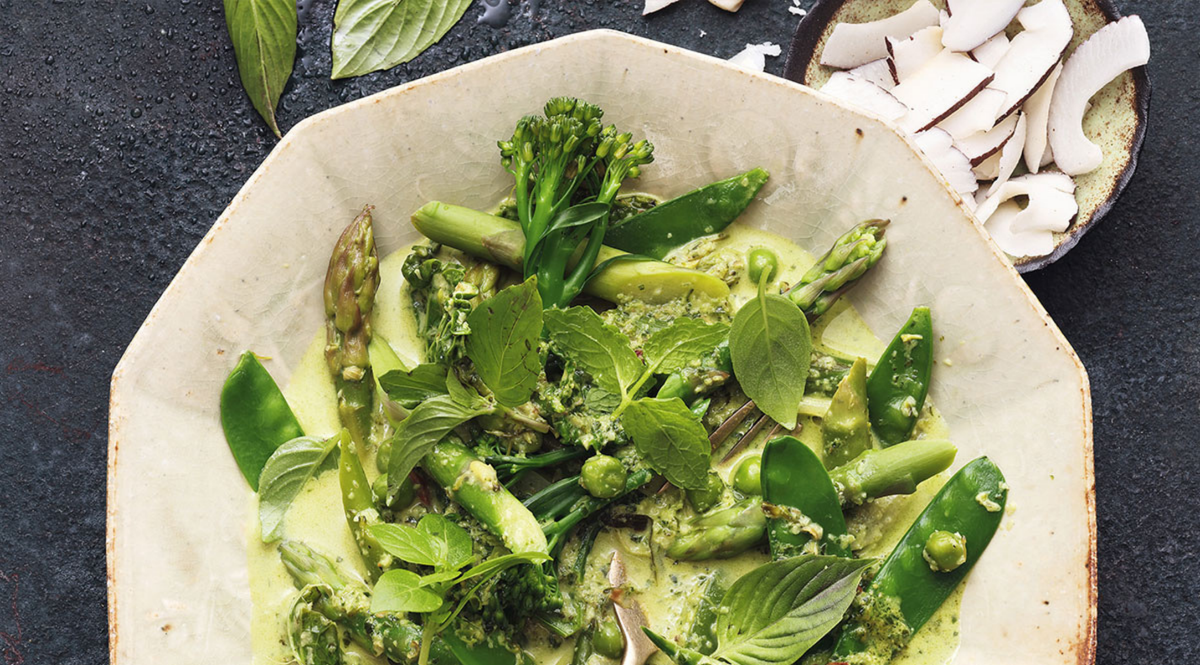 Grünes Gemüsecurry mit Spargel und Broccolini in einer stilvollen Schale, präsentiert auf einer dunklen Oberfläche in Fissler-Qualität.