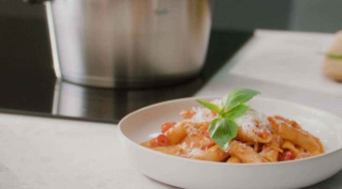 Penne mit Tomatensauce, Käse und Basilikum auf einem Teller neben einem Fissler-Edelstahltopf auf der Arbeitsplatte.