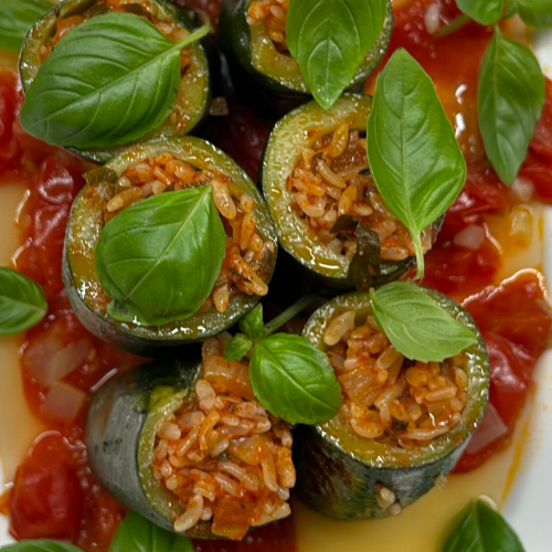 Stuffed zucchini with rice and herbs, garnished with basil on a rich tomato sauce, elegantly presented in high-quality Fissler cookware.