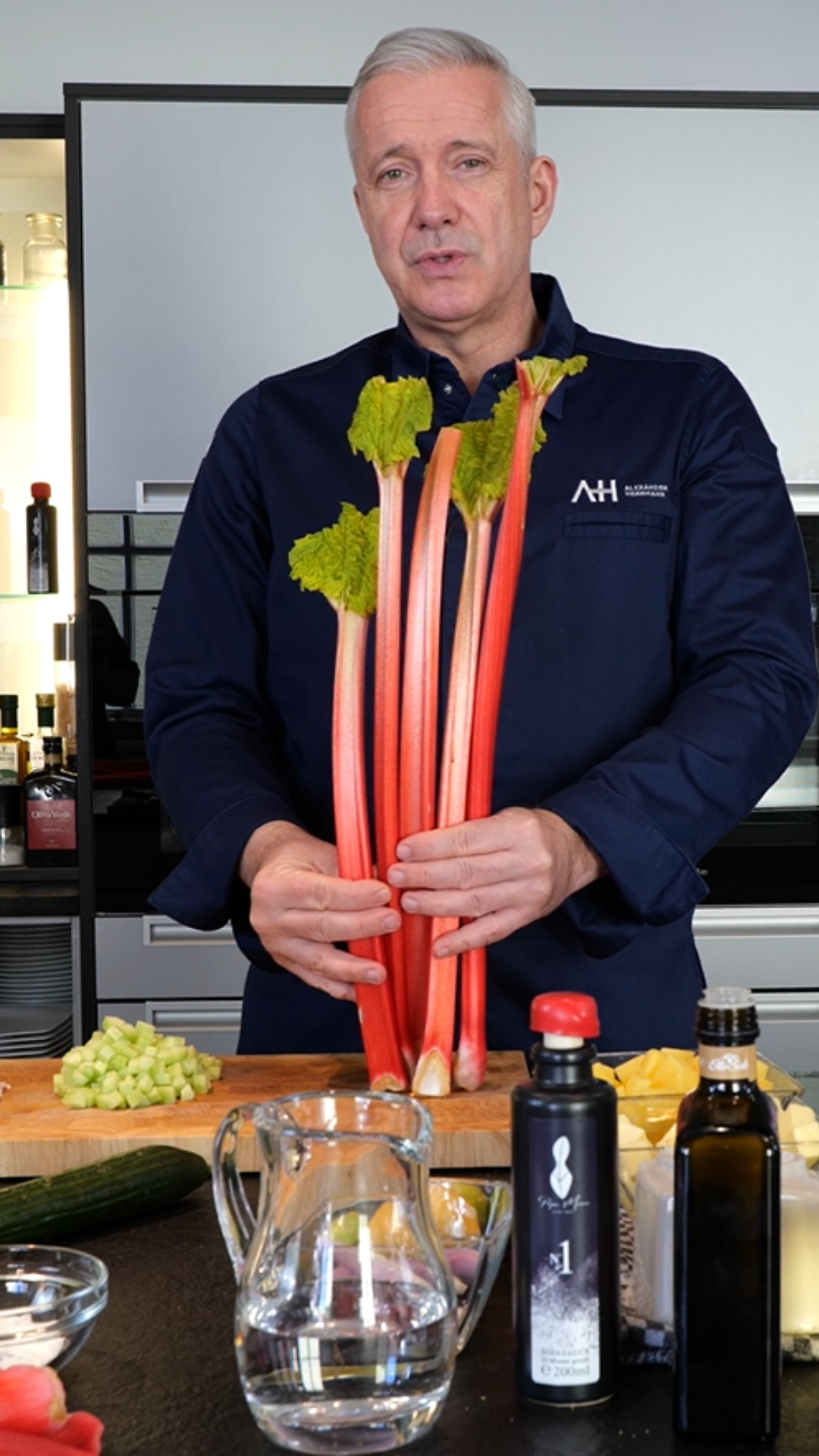 A man in a kitchen with rhubarb, surrounded by chopped ingredients and premium Fissler cookware on the counter.