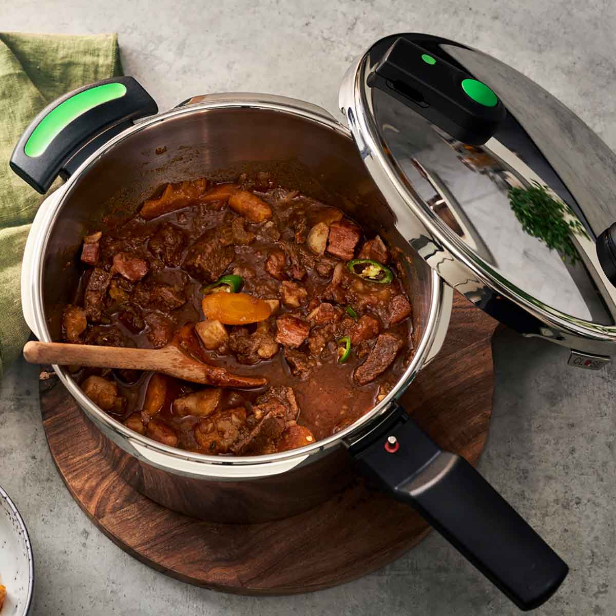 Fissler Vitaquick® Green Schnellkochtopf, offen mit Rindergulasch im Inneren, auf Holzbrett. Deckel daneben; schlankes deutsches Design, nahrhafte Ergebnisse.