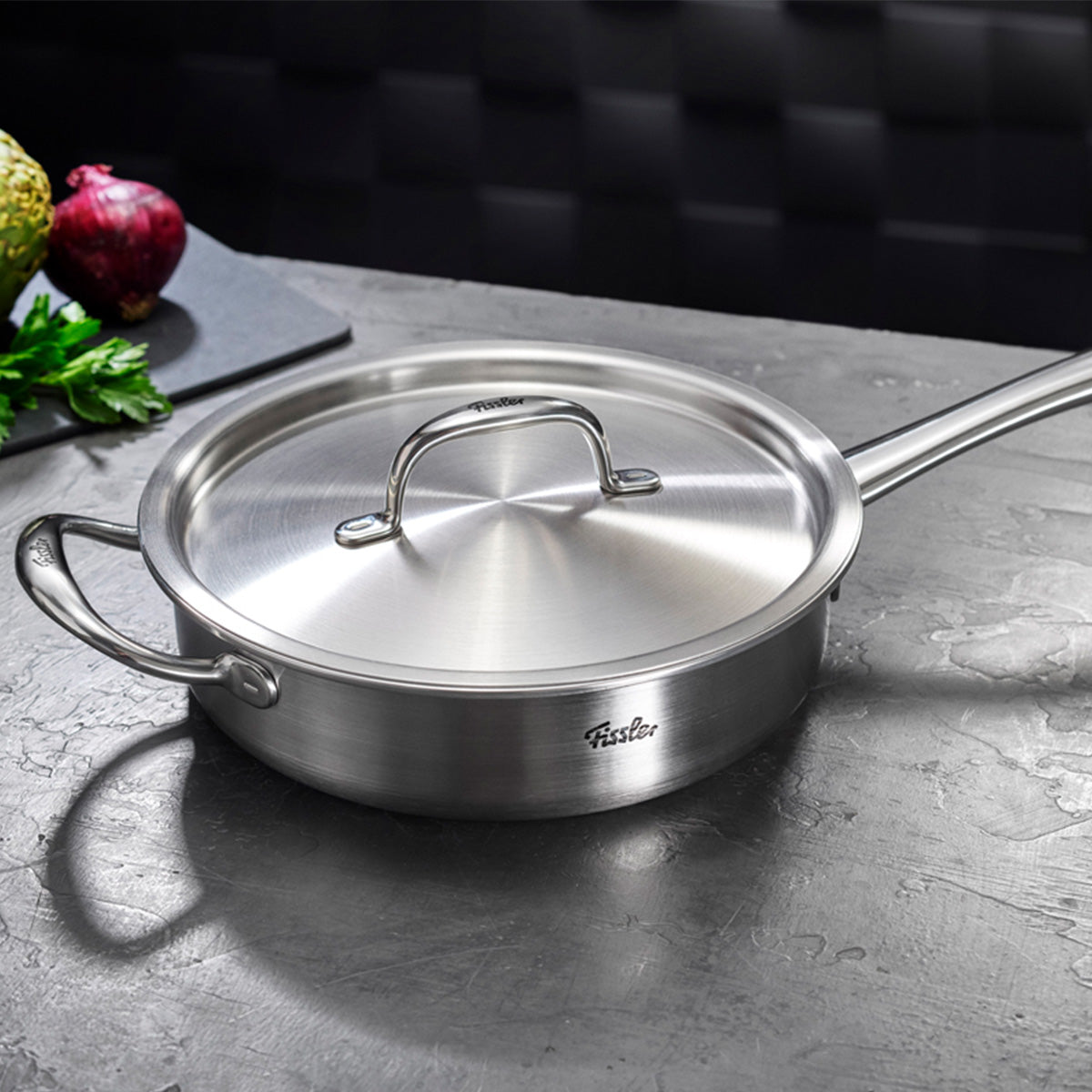 Das 4-teilige Fissler M5 Pro-Ply®-Set mit Metalldeckeln präsentiert sich auf einer grauen Arbeitsfläche. Die aus hochwertigem, recyceltem Edelstahl „Made in Germany“ gefertigten Töpfe zeichnen sich durch zwei solide Griffe und eine edle, gebürstete Metalloberfläche aus – ein Symbol für Fisslers traditionsreiche Präzision und langlebiges Design seit 1845. Im Hintergrund liegt auf einem Schneidebrett frisches Gemüse: Zwiebel, Petersilie und eine Artischocke. Dieses Pfannenset steht für Innovation,